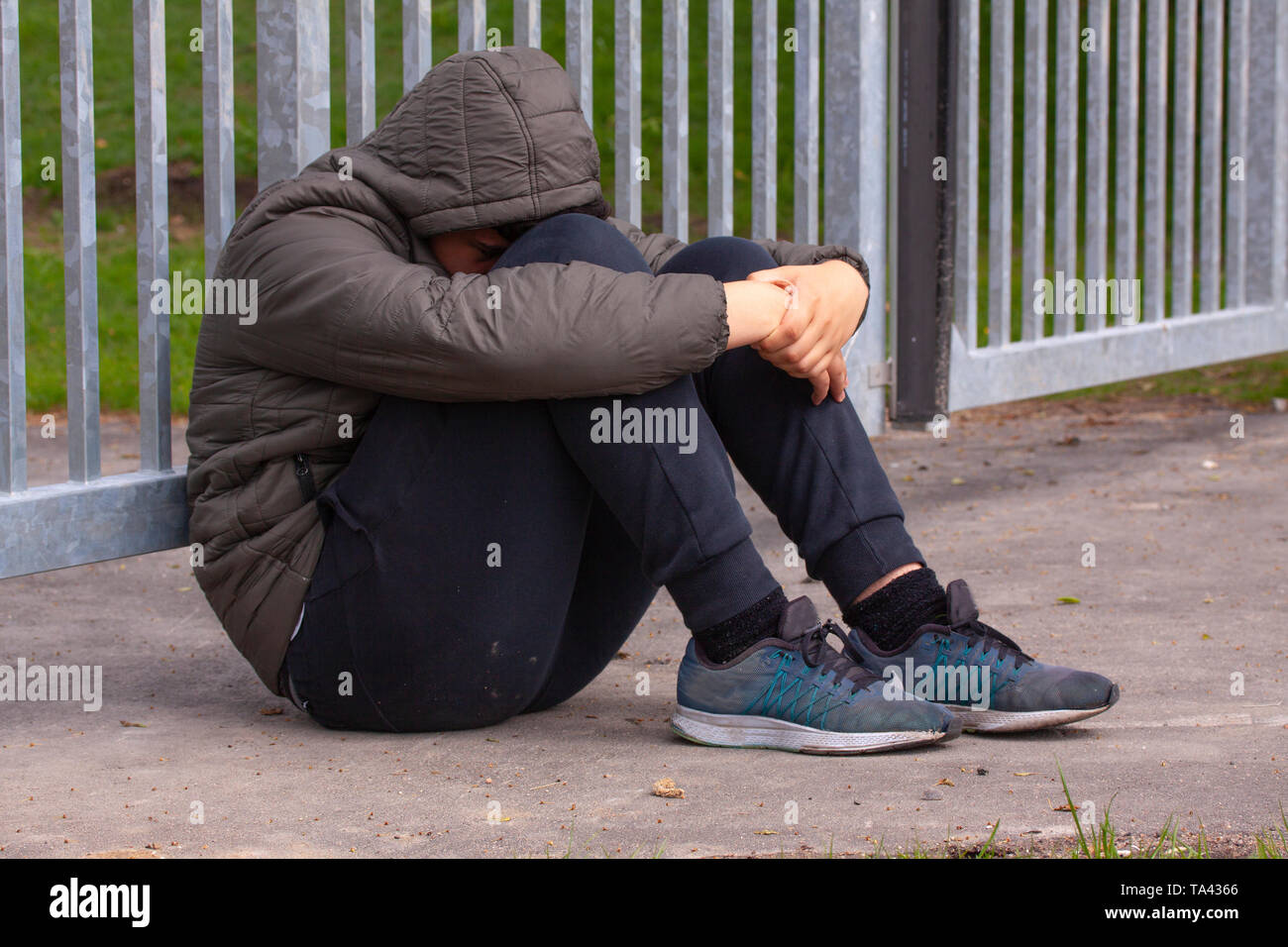 Lonely adolescente seduto da solo al di fuori di una recinzione metallica con barre di ferro. La solitudine e il concetto di bullismo. Foto Stock