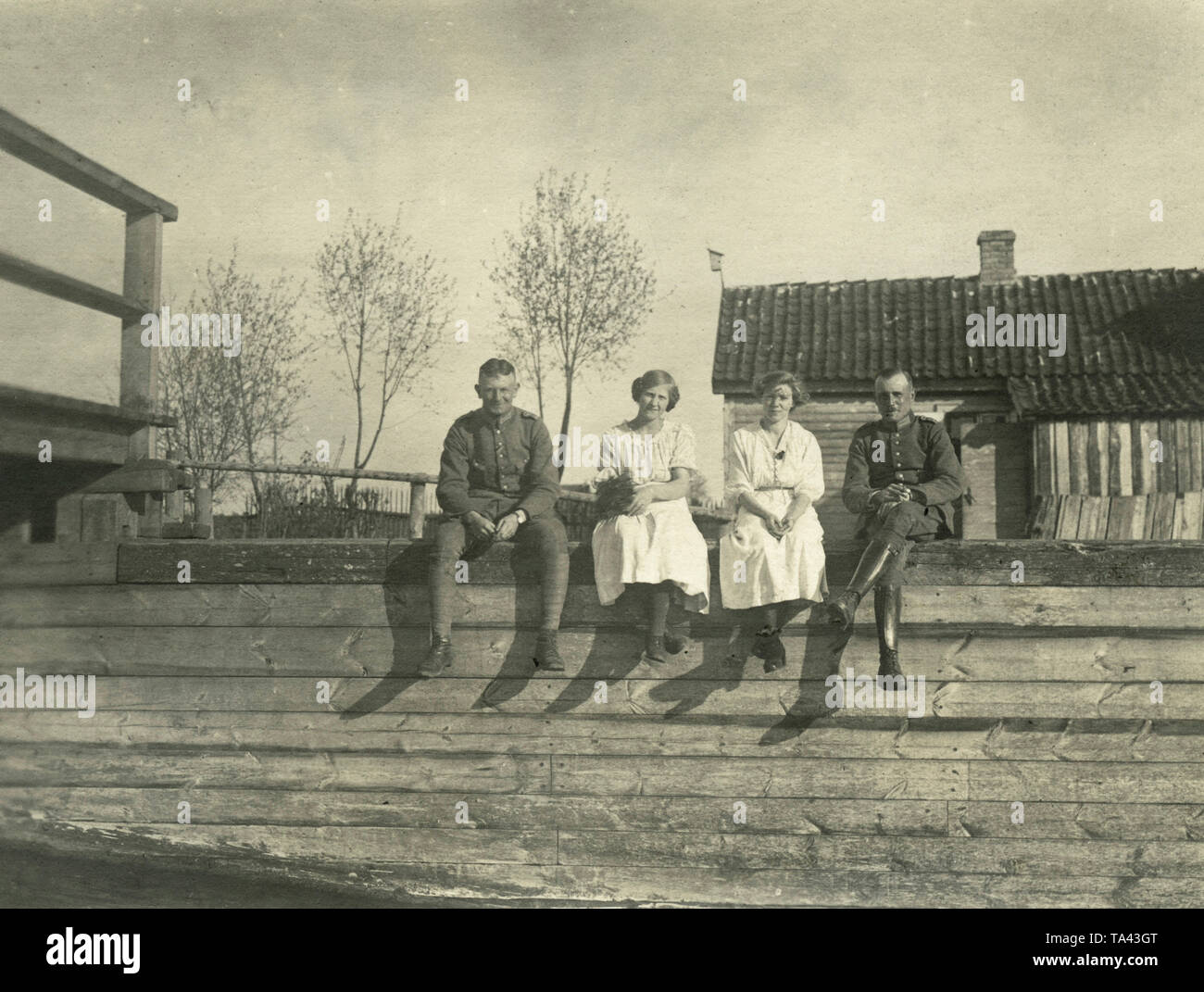 Due soldati del Freikorps " Ferro divisione" (a sinistra: il tenente giordano, destra: Sergente Birkenbihl) sedersi su una staccionata in legno lungo con due donne di famiglie tedesche in Lettonia Jelgava. Foto Stock