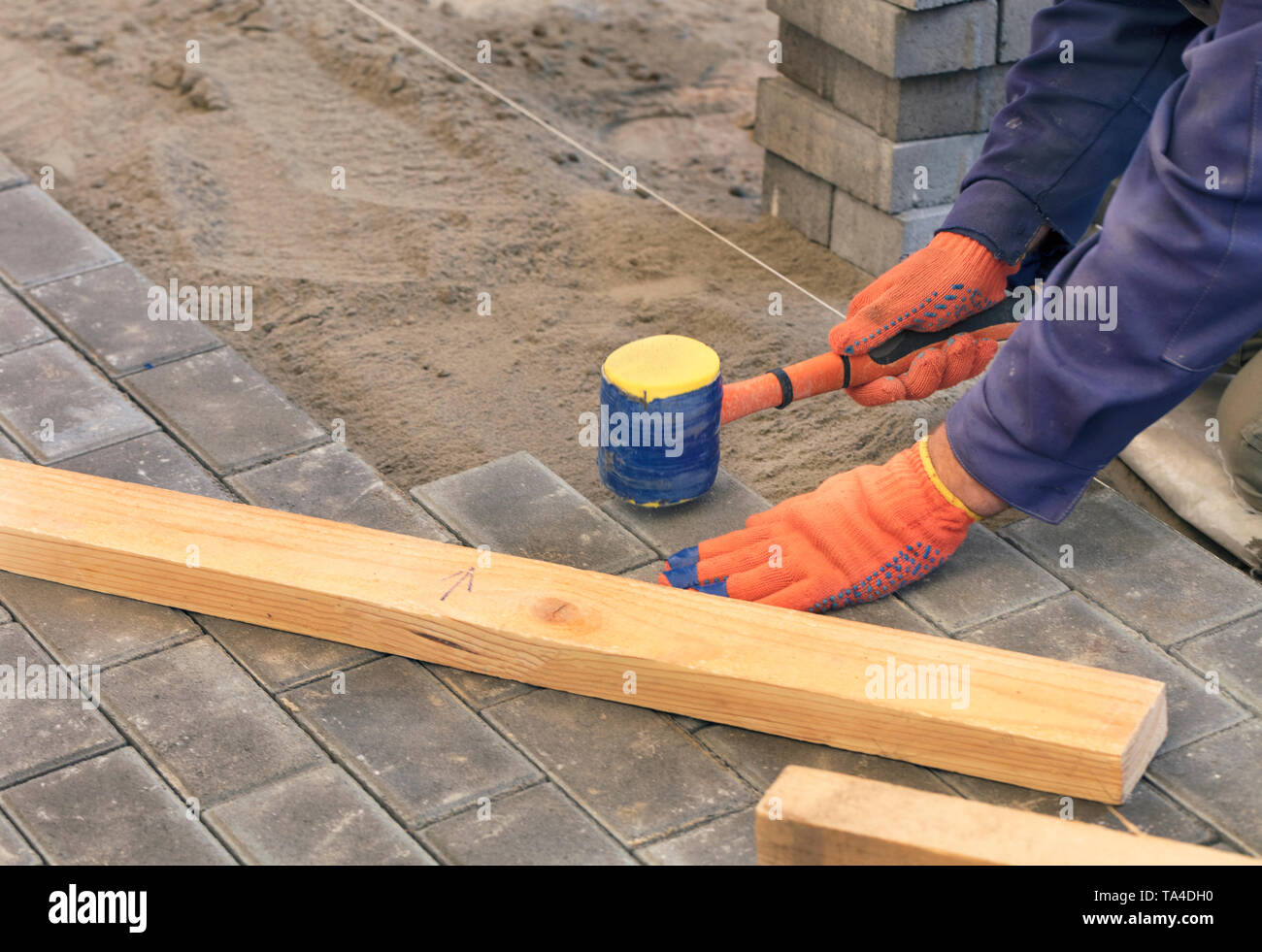 Il lavoratore appoggiare la lastra di pavimentazione con speciali martelli, livellamento secondo il livello del filo teso Foto Stock