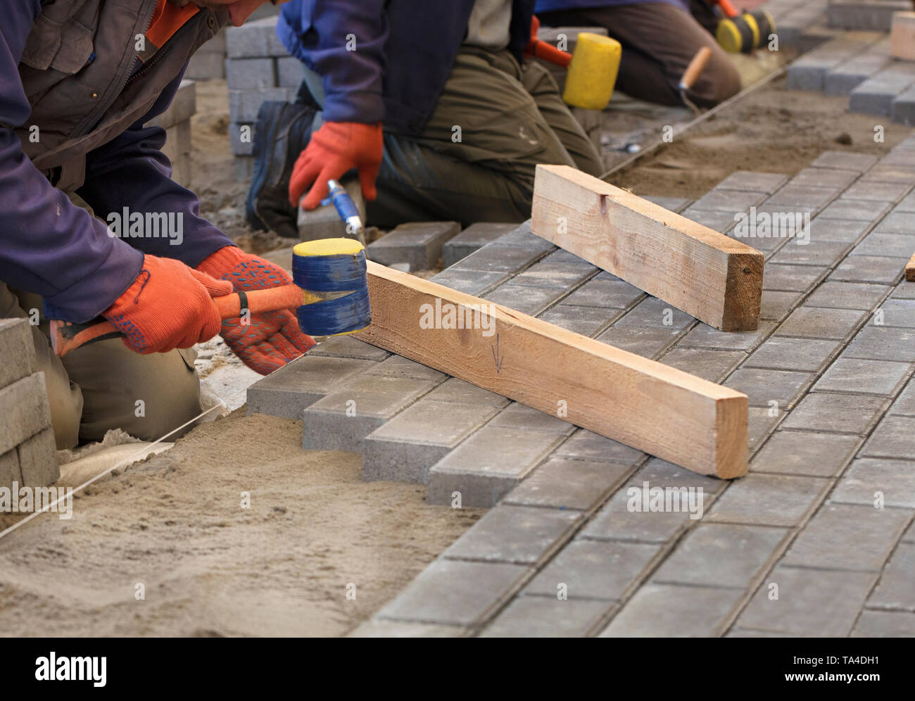 I lavoratori appoggiare la lastra di pavimentazione con speciali martelli, livellamento secondo il livello del filo teso Foto Stock