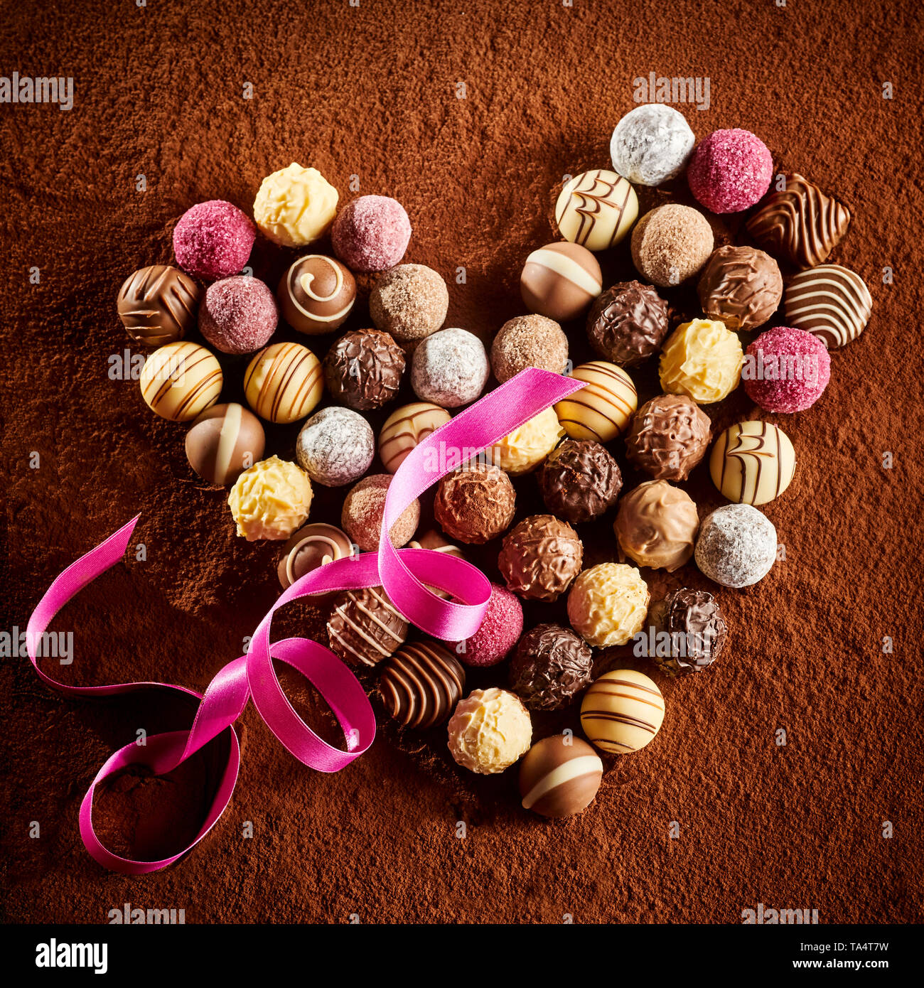 Romantico a forma di cuore ad disposizione dei Bonbons di cioccolato con un twirled nastro rosa su uno sfondo di polvere di cacao in primo piano formato quadrato per Valenti Foto Stock