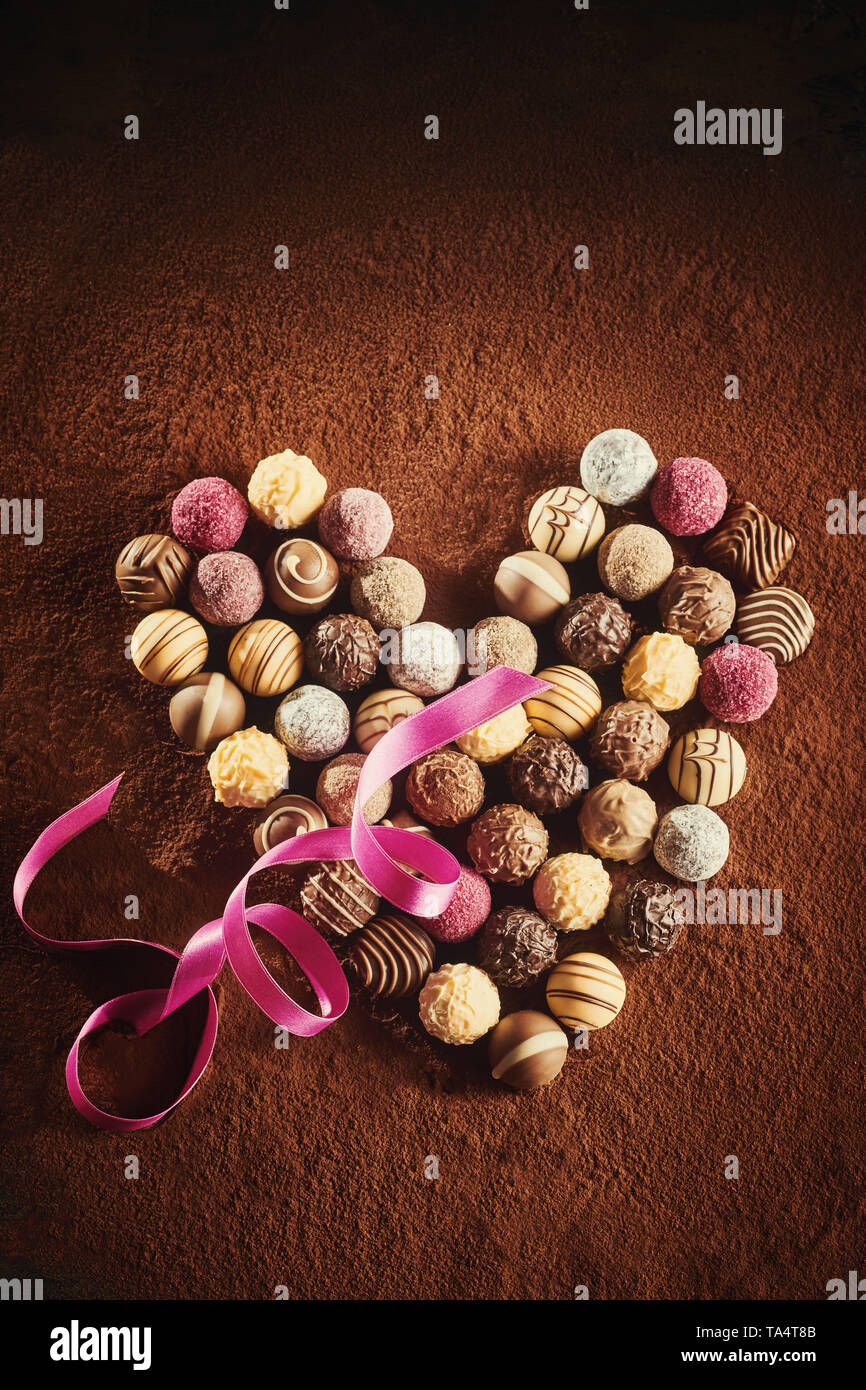 A forma di cuore ad disposizione di lusso fatti a mano cioccolatini sferico su un letto di polvere di cacao con un twirled nastro rosa per un sweetheart su Valentines d Foto Stock