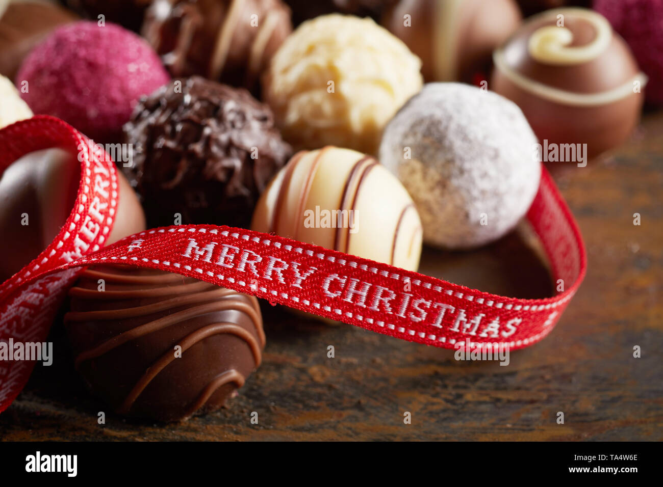 Luxury Chocolate Merry Christmas Festive sfondo con un nastro rosso recante il messaggio di saluto festivo intrecciati su un assortimento di specialità di sfere di cioccolato Foto Stock