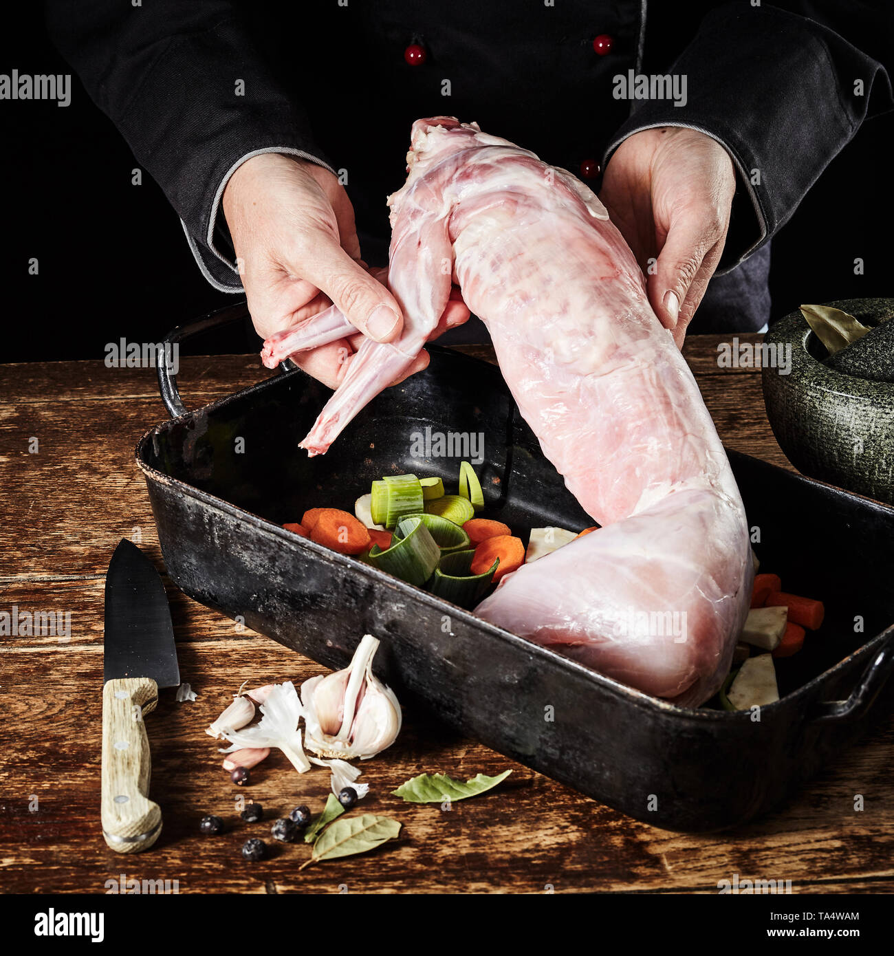 Lo Chef visualizzando un crudo fresco di coniglio selvatico la carcassa come egli lo prepara per la tostatura in un tegame con porri e carote, aglio, erbe e spezie Foto Stock