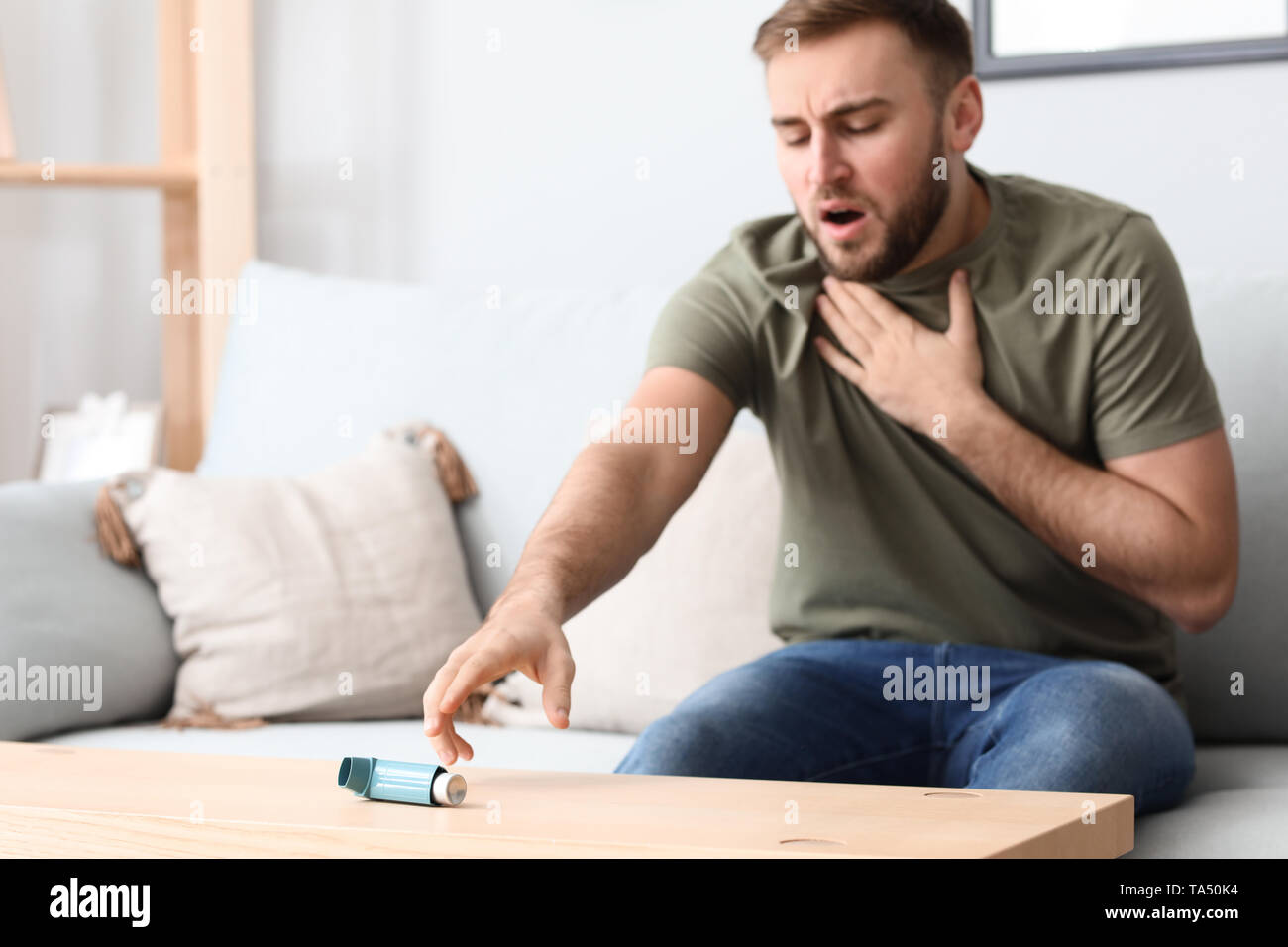 Giovane uomo con attacchi di asma tenendo inalatore dalla tabella Foto Stock