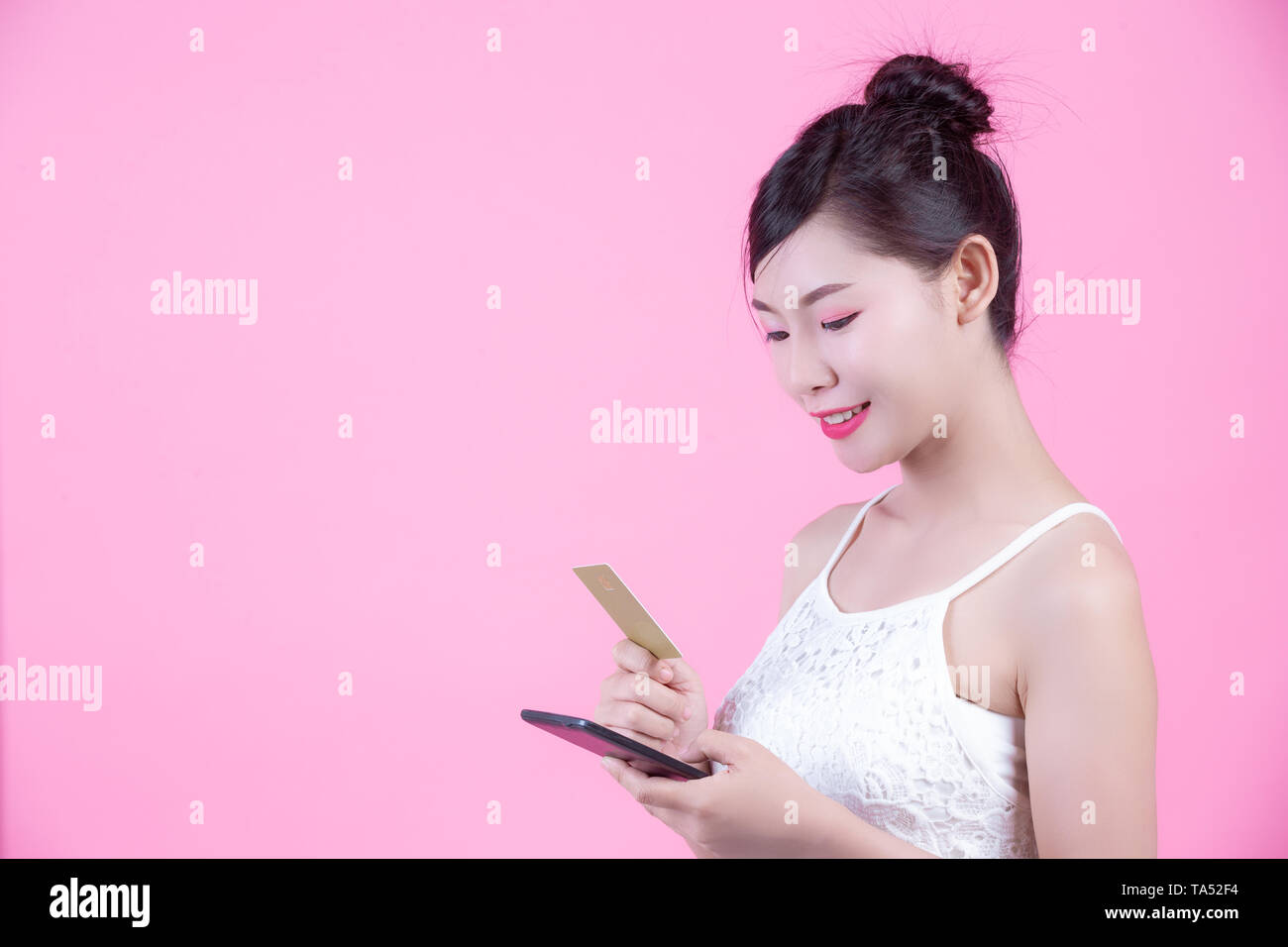 Bella donna tenendo un smartphone e scheda su un sfondo rosa Foto Stock