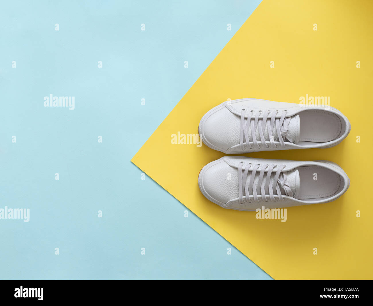 Bianco Pelle sneakers su blu e sfondo giallo. Coppia di moda bianco alla moda scarpe da ginnastica o sneakers con copia spazio per testo in backgr colorati Foto Stock