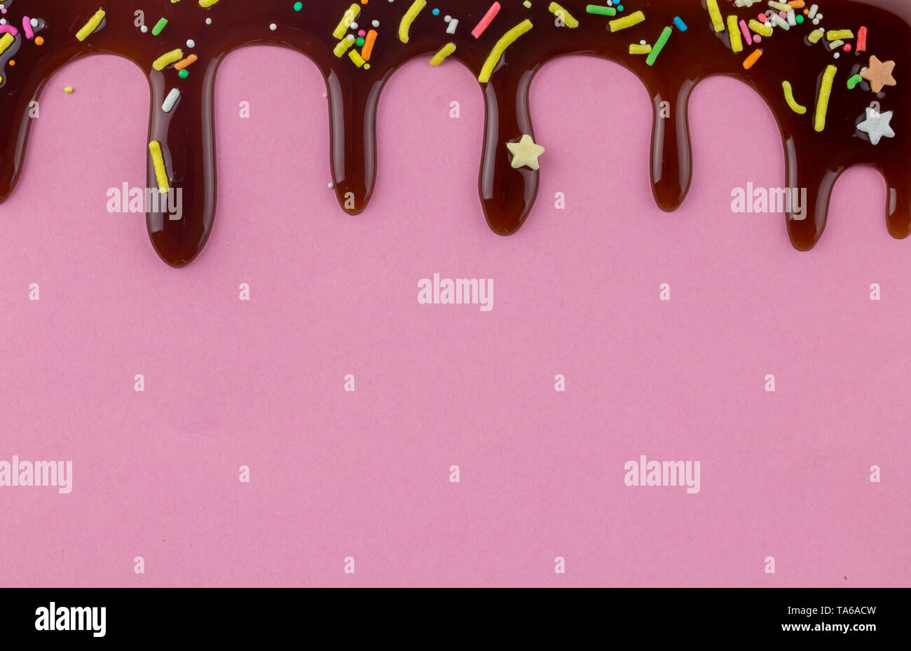 Torta topping spruzzi di colore con il cioccolato che scorre verso il basso su sfondo rosa - spazio per il testo Foto Stock