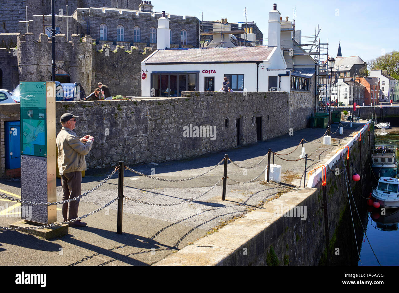 Un vecchio uomo in procinto di prendere una fotografia di Castletown harbour con caffè Costa e il castello in background Foto Stock