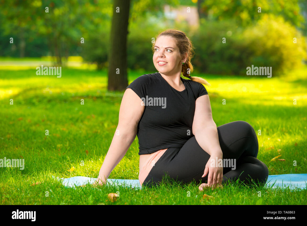 Ritratto di un plus modello dimensioni nel parco durante una lezione di yoga, stretching esercizio Foto Stock