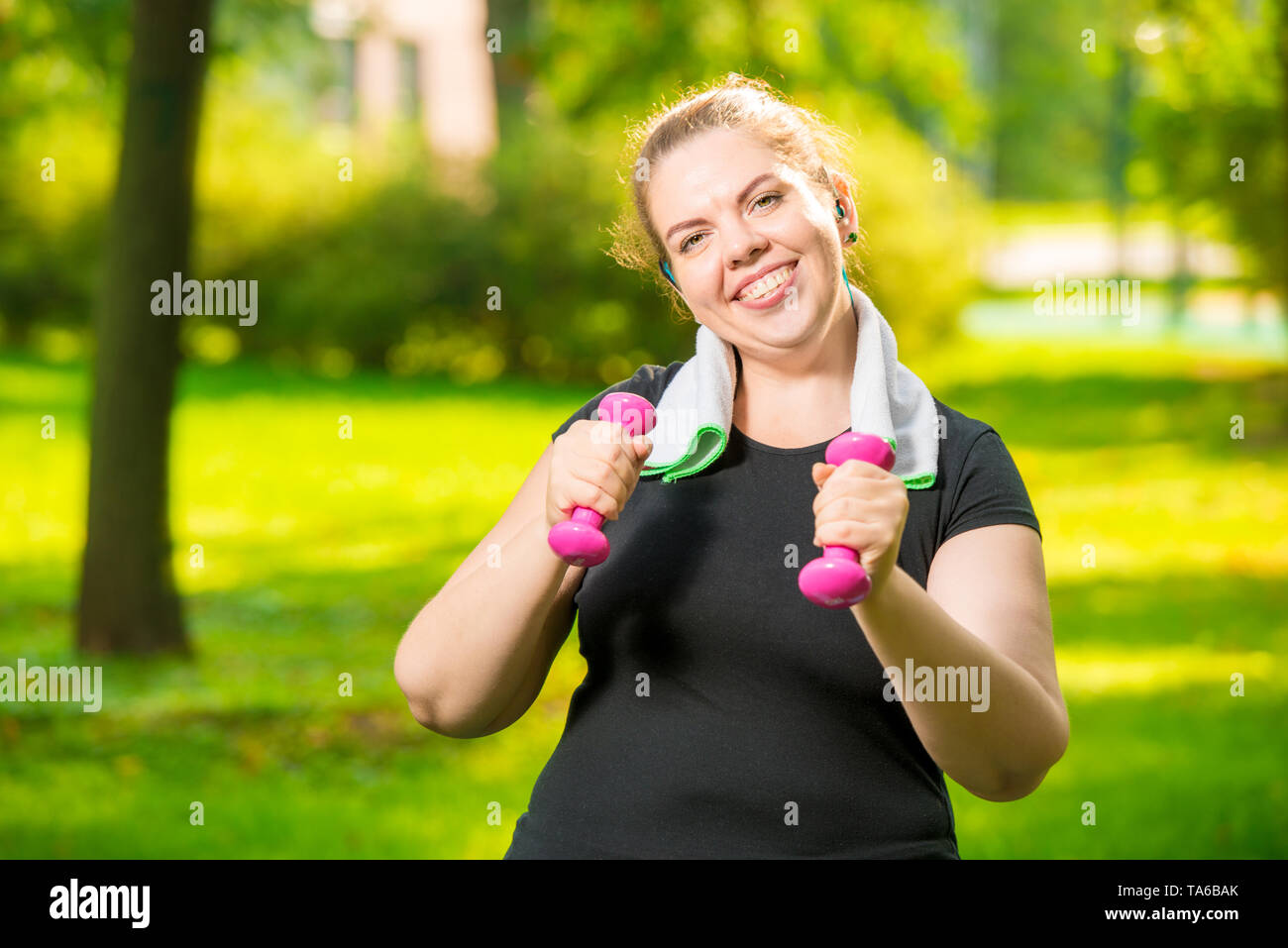 Felice donna grassa con manubri nel parco durante gli allenamenti Foto Stock