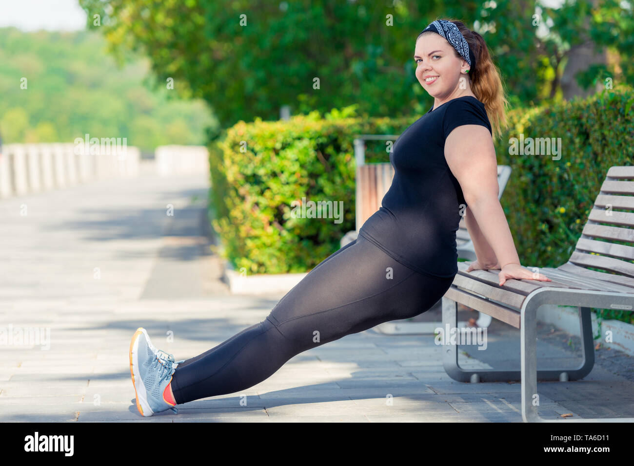 Felice donna grassa esegue gli esercizi del parco su un banco di lavoro Foto Stock