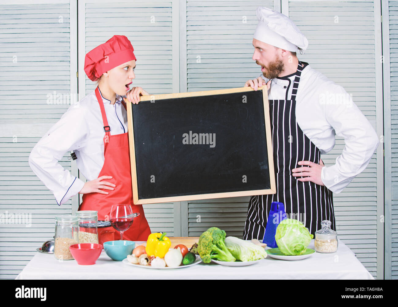 Guadagnando una gamma di competenze. Paio di uomo e donna azienda lavagna vuota nella scuola di cucina. Master cucinare e cuocere prep dando lezioni di cucina. Chef e cuoco insegnamento helper master class, copia dello spazio. Foto Stock