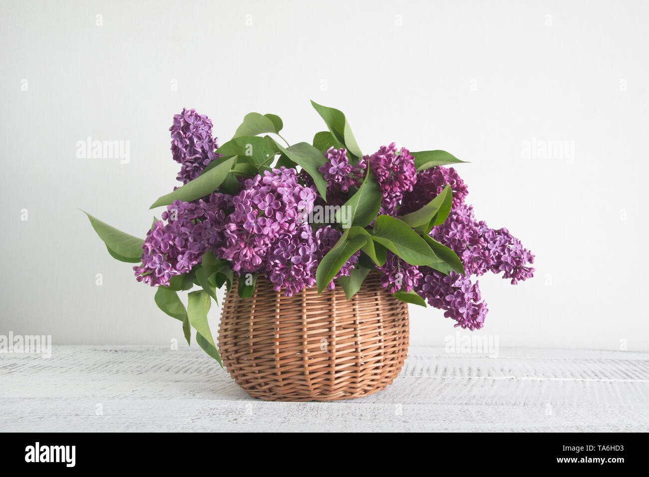 Cesto di fiori lilla sul bianco sullo sfondo di legno. Retrò tonica. Madri e womens giorno. Foto Stock