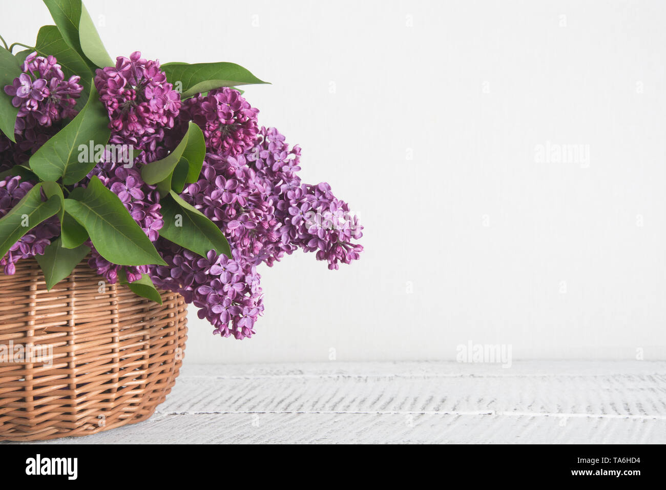 Cesto di fiori lilla sul bianco sullo sfondo di legno. Retrò tonica. Madri e womens giorno. Spazio per il testo. Foto Stock