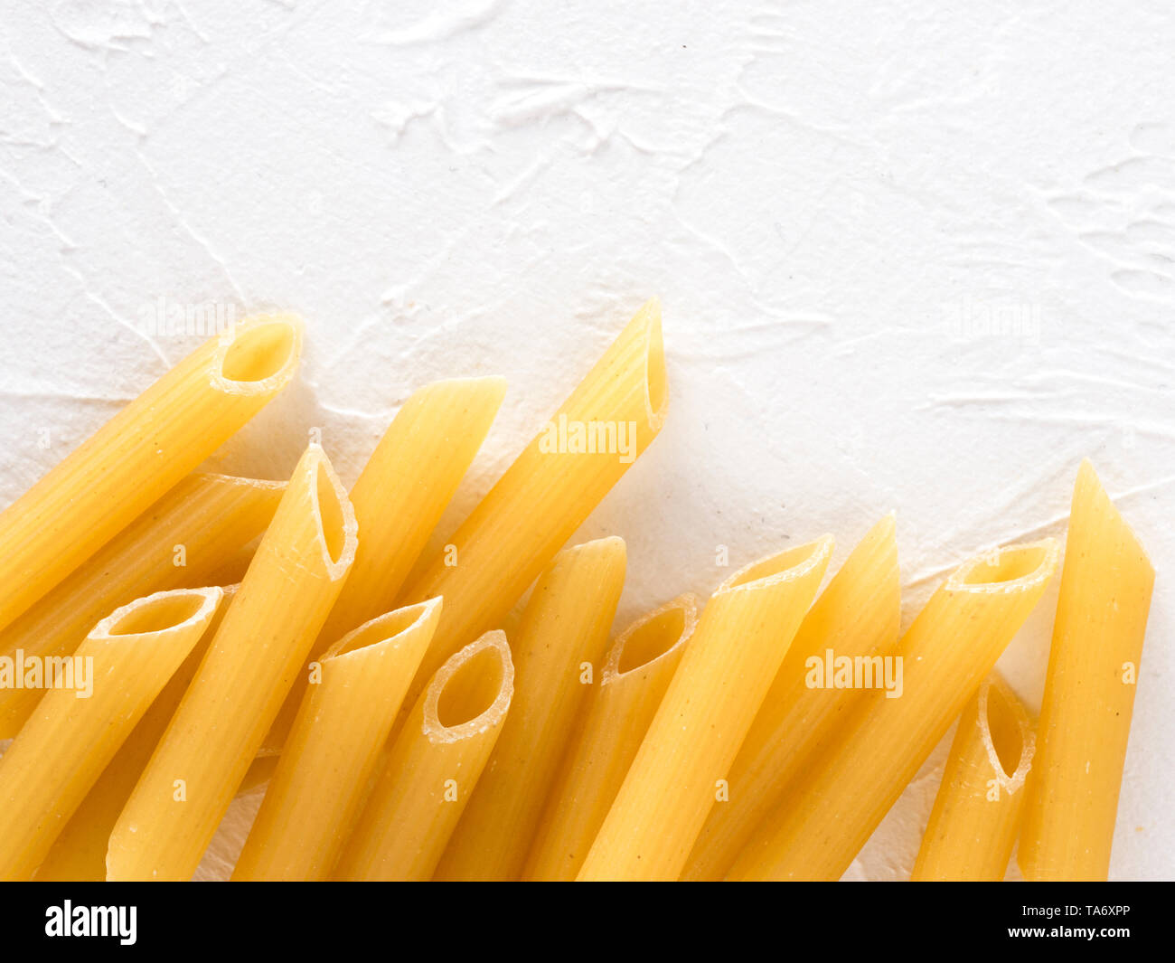 La pasta grezza come sfondo di cibo. Italian Penne Rigate Maccheroni testurizzato su sfondo bianco. La pasta secca selezione vicino. Vista superiore o laici piana w Foto Stock