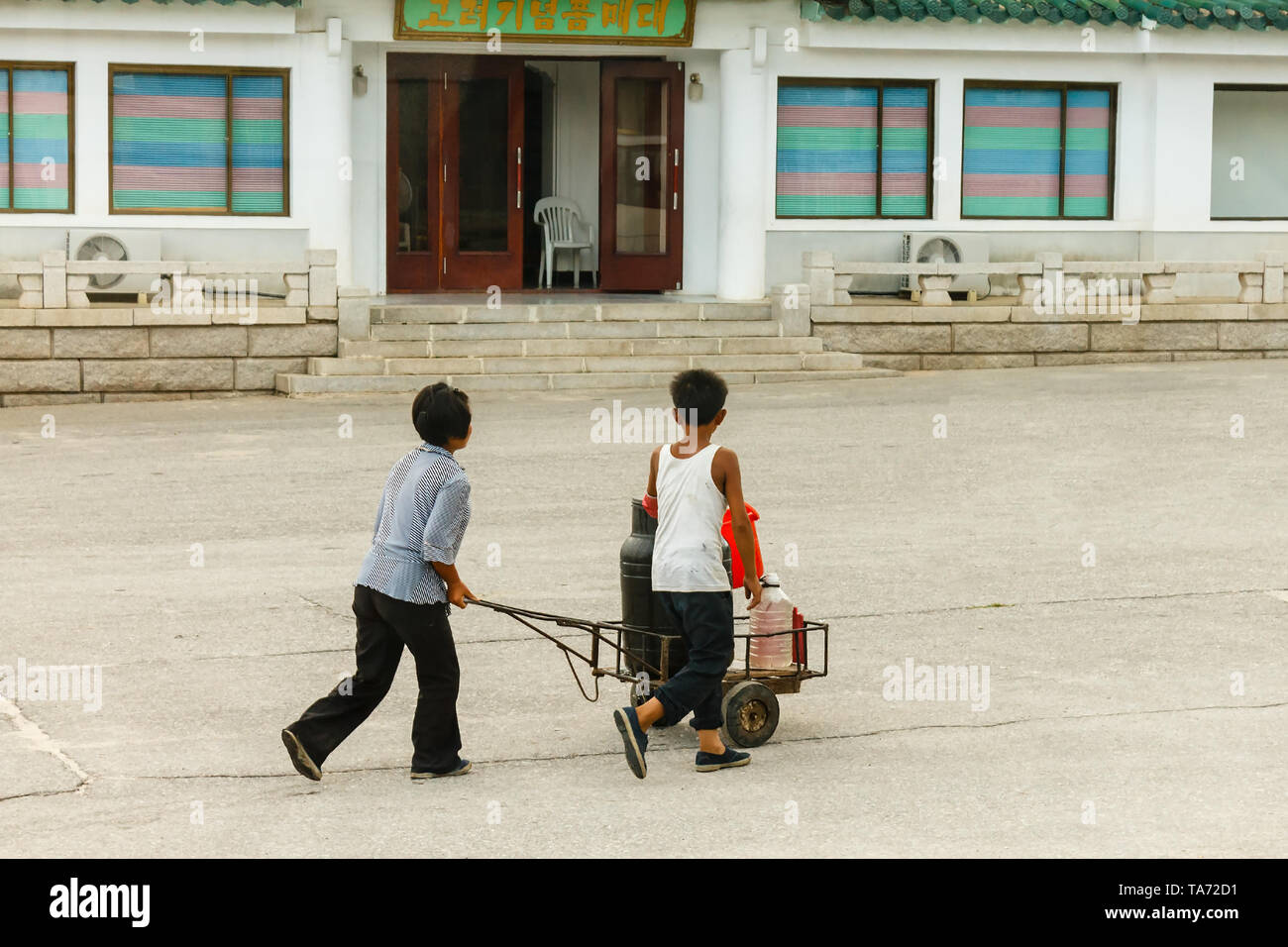 Kaesong, Nord Korea-July 30, 2014: nord coreano donna con un ragazzo su un carrello porta un barile di acqua. Foto Stock