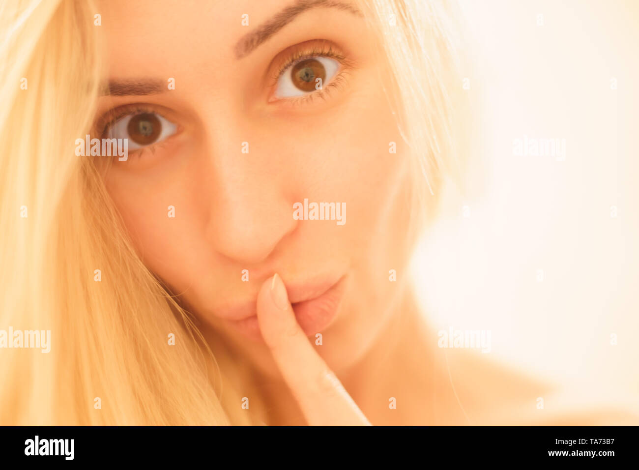 Ritratto di una bella ragazza giovane closeup faccia mostra il silenzio gesto con il dito sulla sua labbra isolate su sfondo chiaro Foto Stock