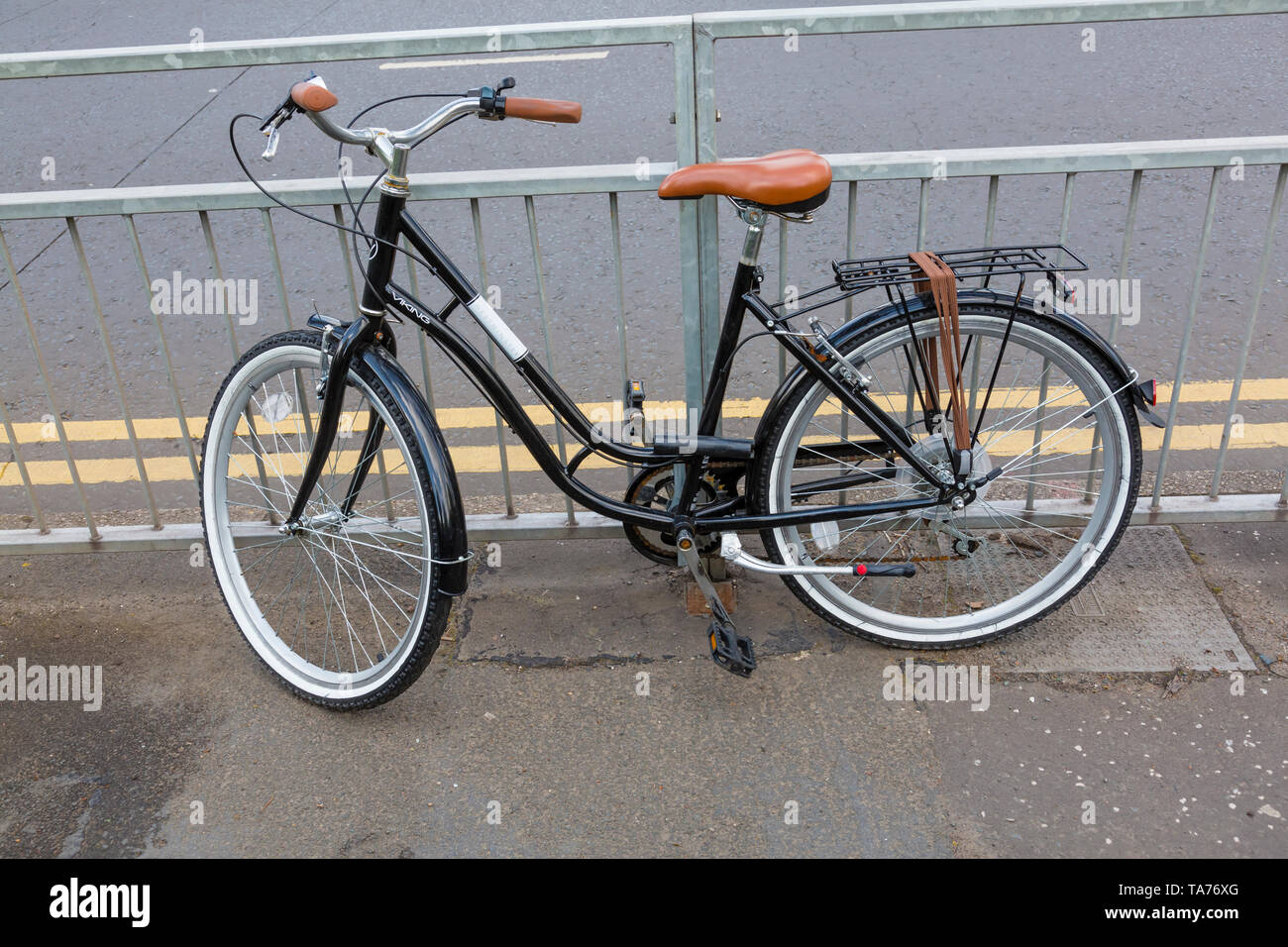 Una bicicletta nero parcheggiato contro le ringhiere su un marciapiede accanto a una strada, REGNO UNITO Foto Stock