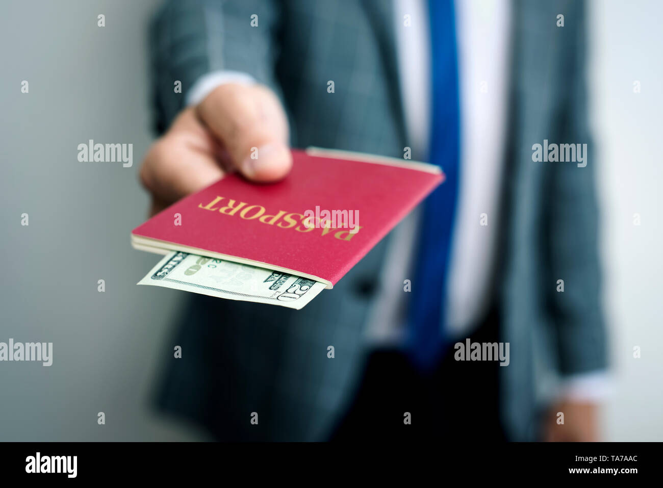 Primo piano di un giovane imprenditore caucasico, indossando un elegante abito grigio, con il suo passaporto in mano, con una 20 dollari banconota in esso Foto Stock