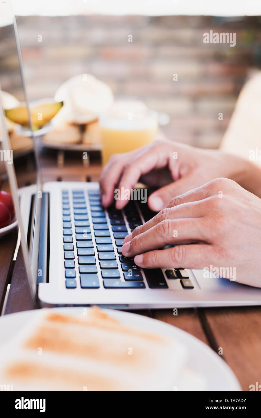 Primo piano di un giovane uomo caucasico usando un computer portatile seduti ad un tavolo di legno all'aperto durante un pasto Foto Stock