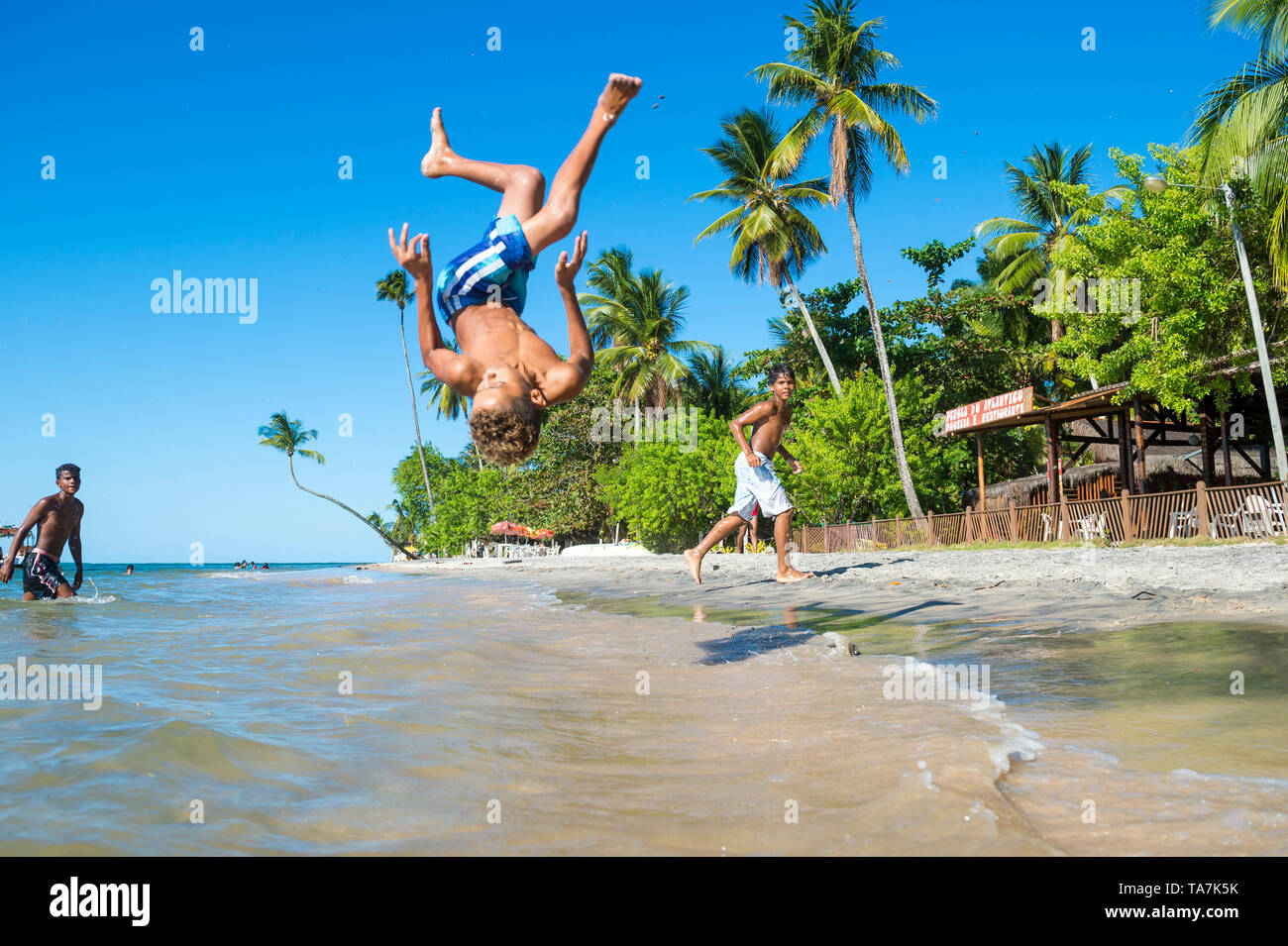 CAIRU, Brasile - Marzo 2018: i giovani brasiliani si alternano facendo capriole e acrobatico si tuffa nel mare sulla riva della spiaggia del villaggio. Foto Stock