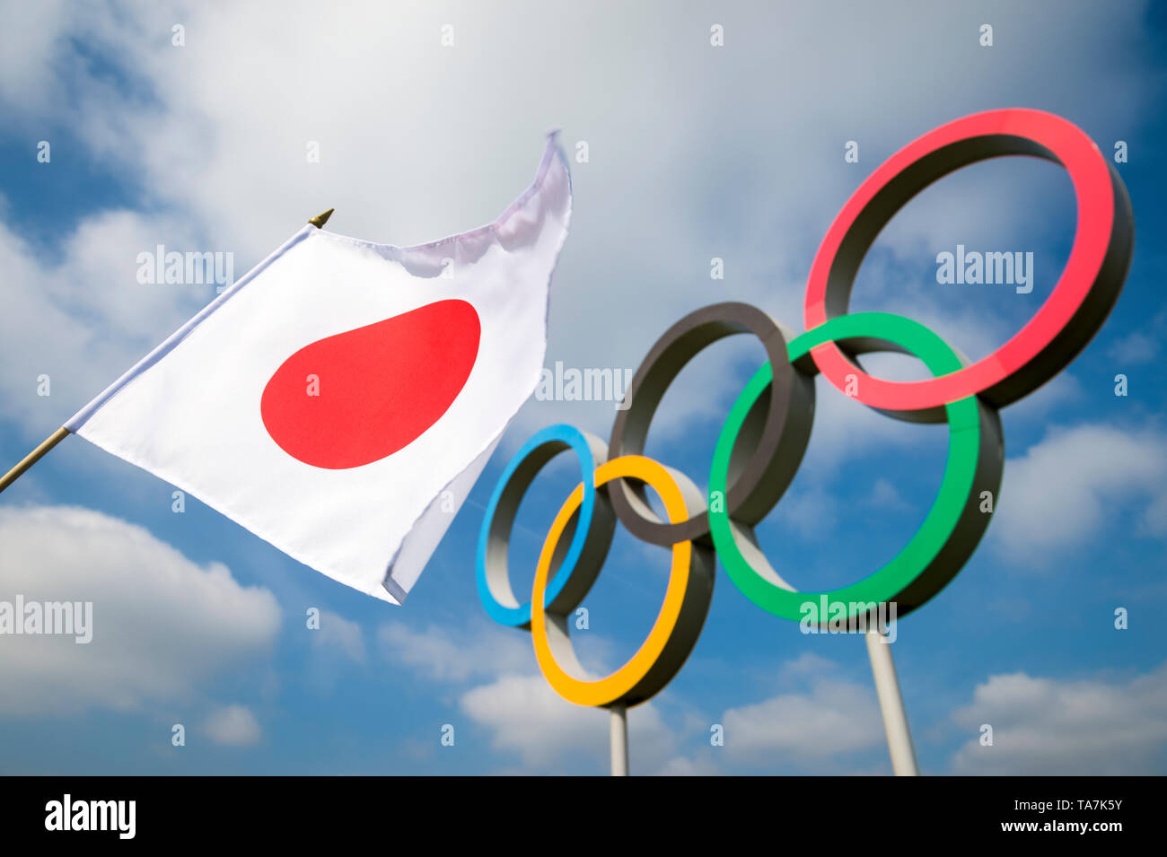 Londra - Aprile 2019: una bandiera giapponese sventola al vento nella parte anteriore di anelli olimpici in piedi sotto il luminoso cielo blu. Foto Stock