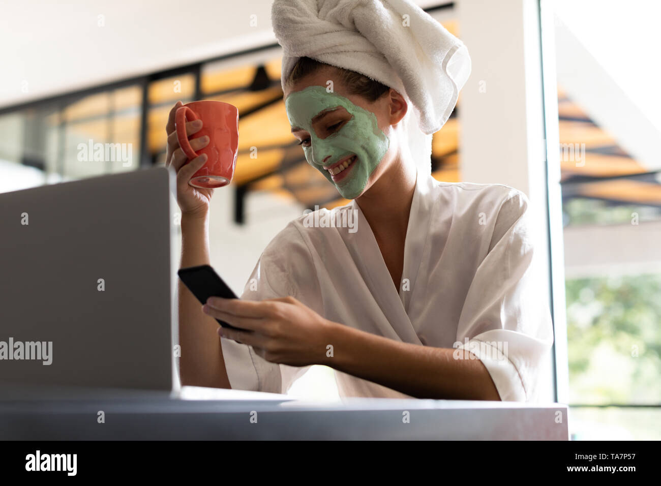 Donna in accappatoio controllando il suo telefono mentre un caffè Foto Stock