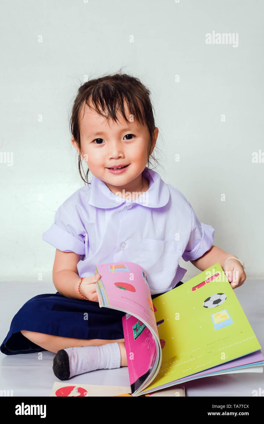 Bambina la lettura di un libro ha in età prescolare che indossano uniformi di scuola in casa. Foto Stock
