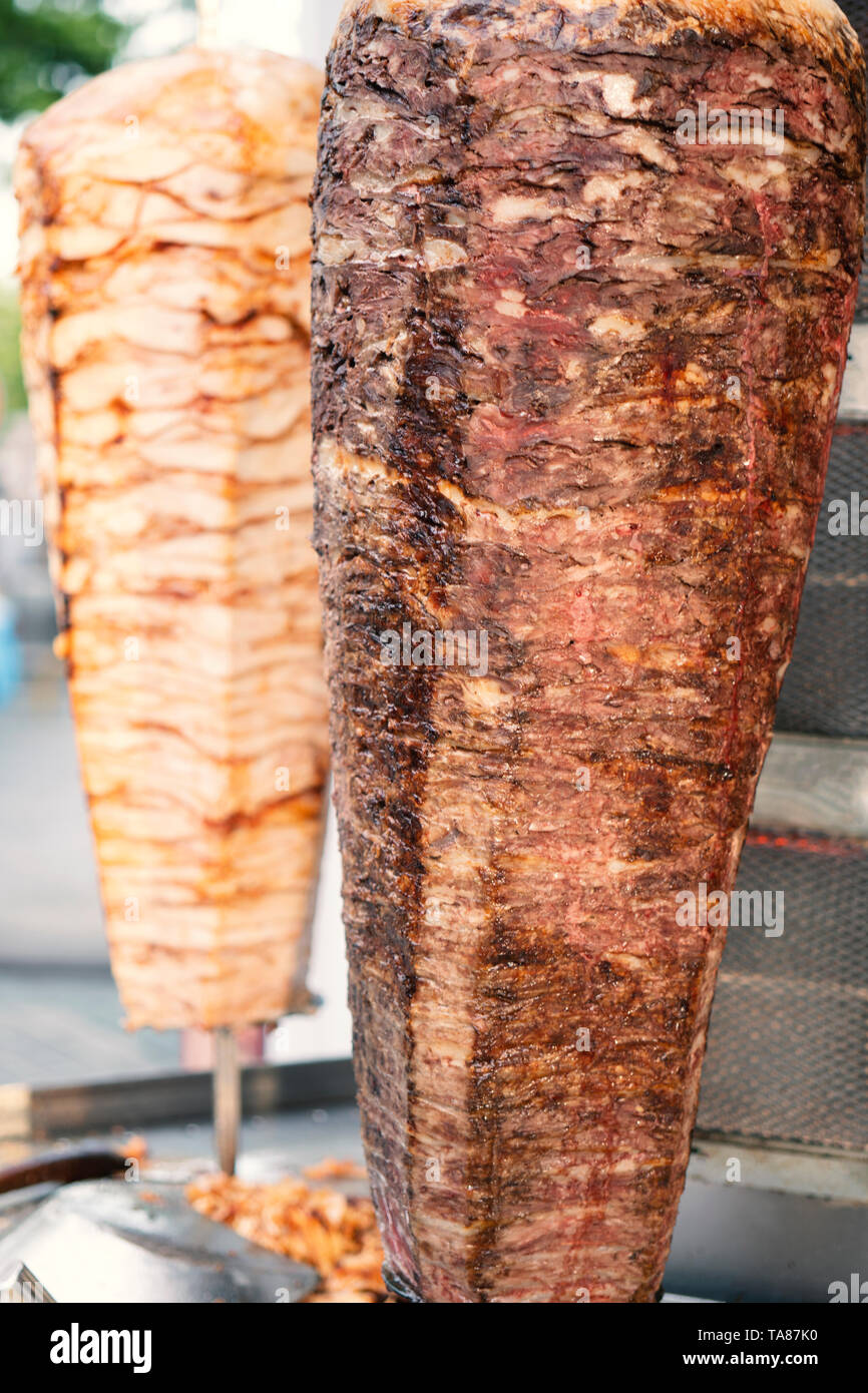 Due ruotando spiedini di pollo e carne di agnello alla griglia in acciaio inox grill e pronto a servire in una tipica del Medio Oriente il fast food kebab panino Foto Stock