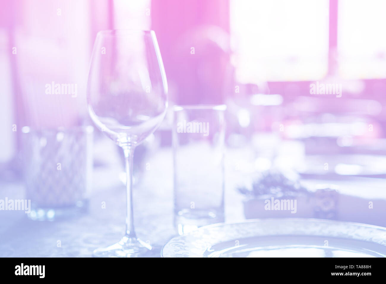 Bicchiere di vino alla celebrazione e tavolo da pranzo impostazione con decorazioni floreali su luce rosa blu gradiente dello sfondo. Foto Stock