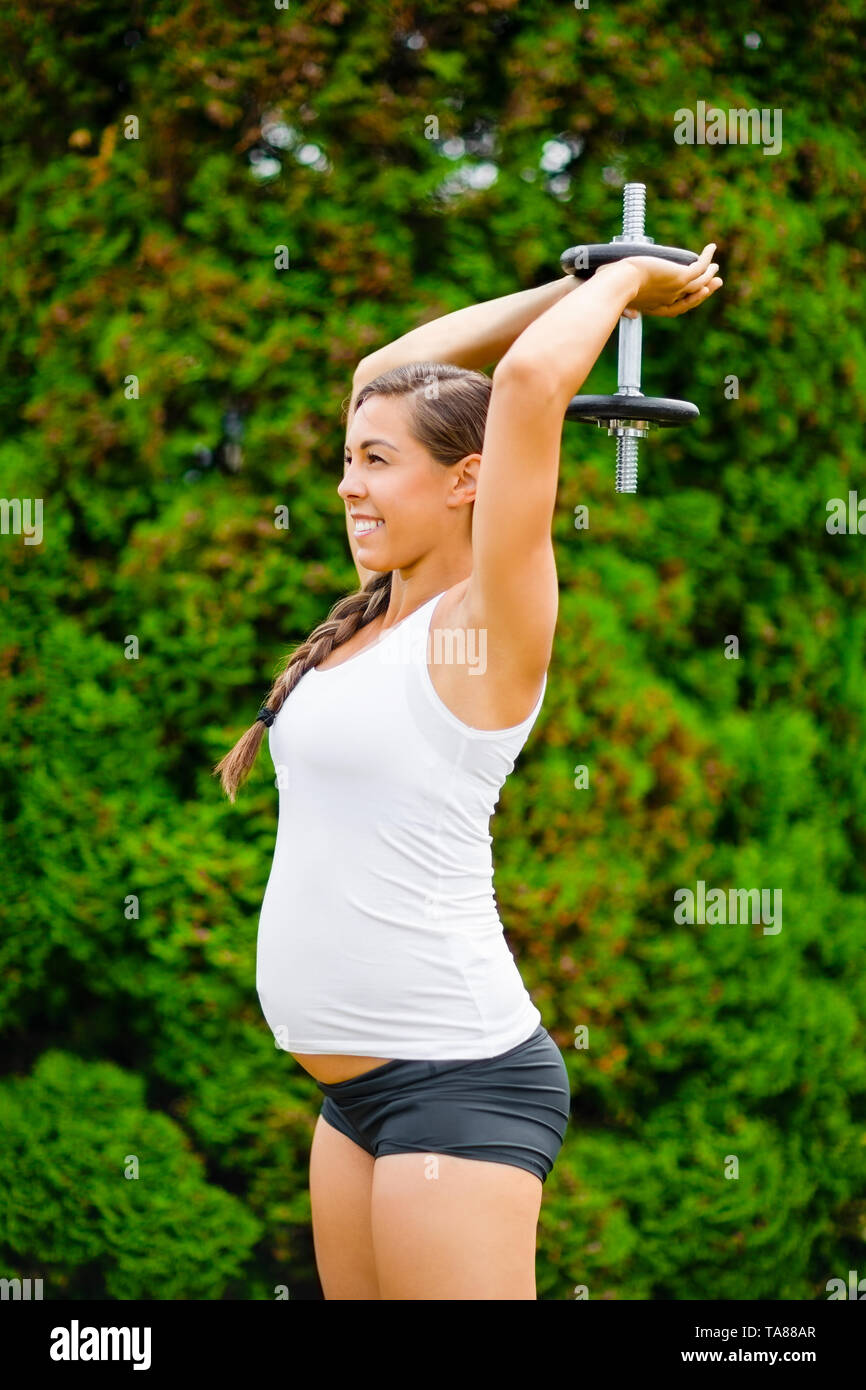 Donna incinta eseguendo tricipiti esercizio di estensione in posizione di parcheggio Foto Stock