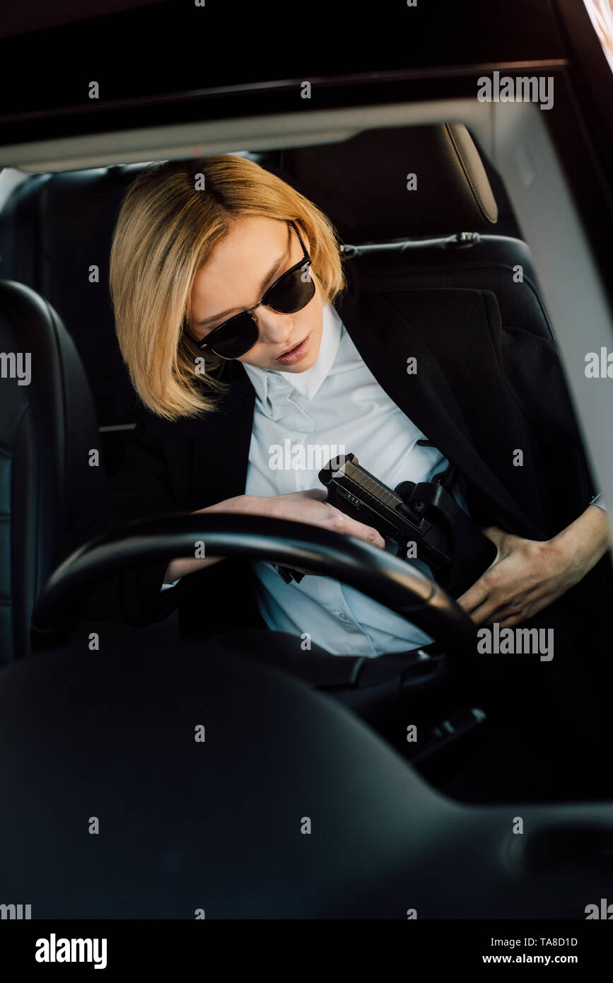 Giovane e bella donna bionda in occhiali da sole tenendo la pistola in auto Foto Stock