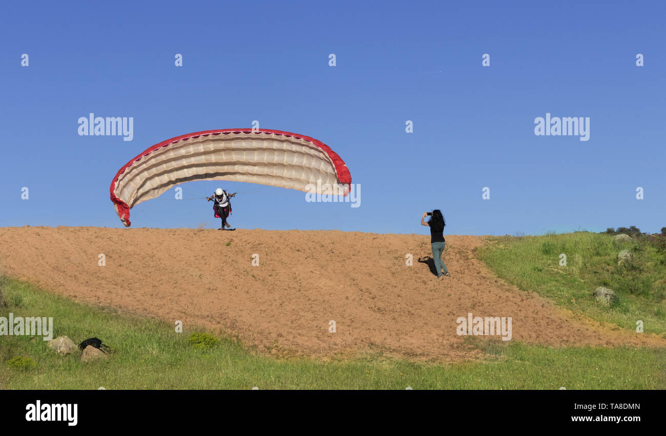 Femmina pilota di parapendio in decollo e la donna le riprese con il suo mobile, con un cielo blu in background Foto Stock