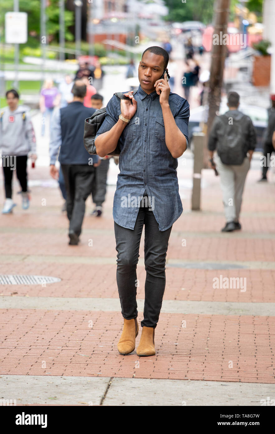 Giovane Africano Americano di Philadelphia, camminando sul Tempio campus universitari sul suo telefono cellulare Foto Stock