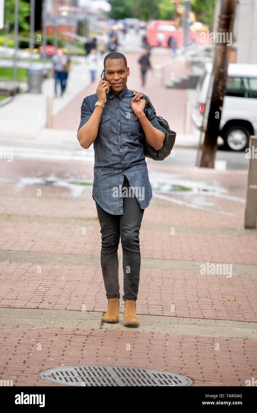 Giovane Africano Americano di Philadelphia, camminando sul Tempio campus universitari sul suo telefono cellulare Foto Stock