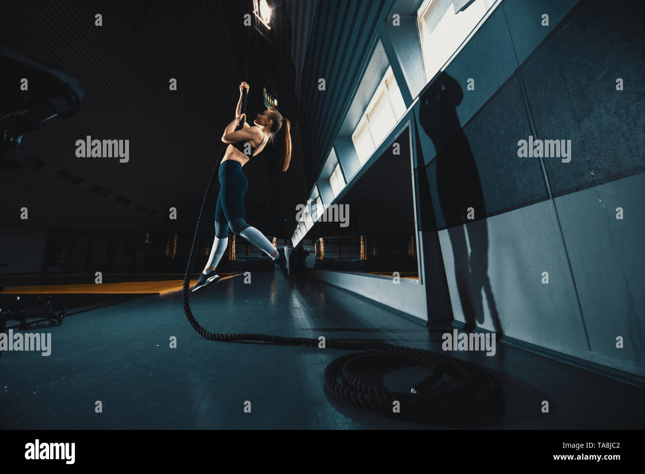 A piena lunghezza ampia angolazione di una donna di eseguire la corda si arrampica in palestra. Copyspace sfondo con atletica composizione sani. Crossfit e fitne Foto Stock