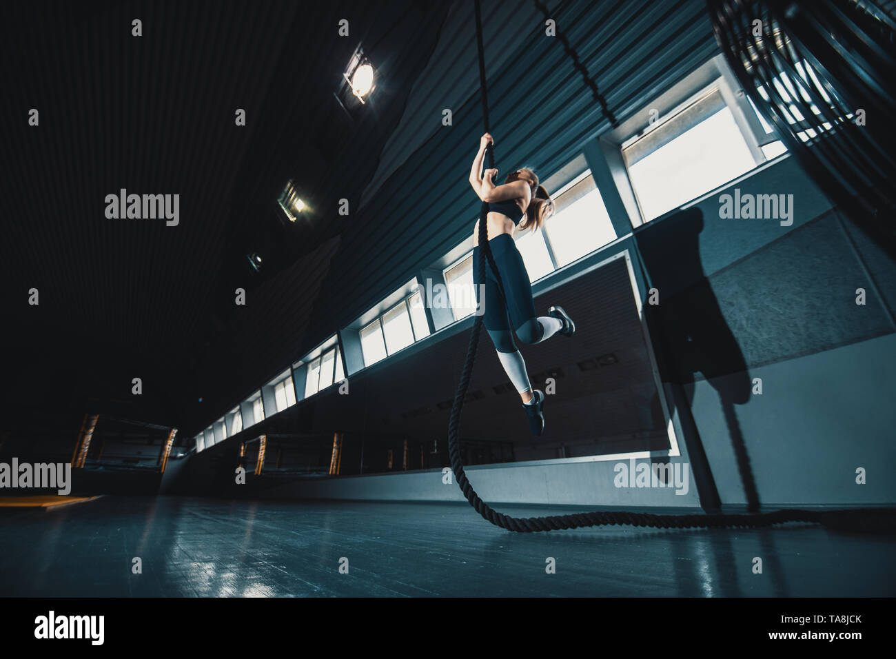 A piena lunghezza ampia angolazione di una donna di eseguire la corda si arrampica in palestra. Copyspace sfondo con atletica composizione sani. Crossfit e fitne Foto Stock