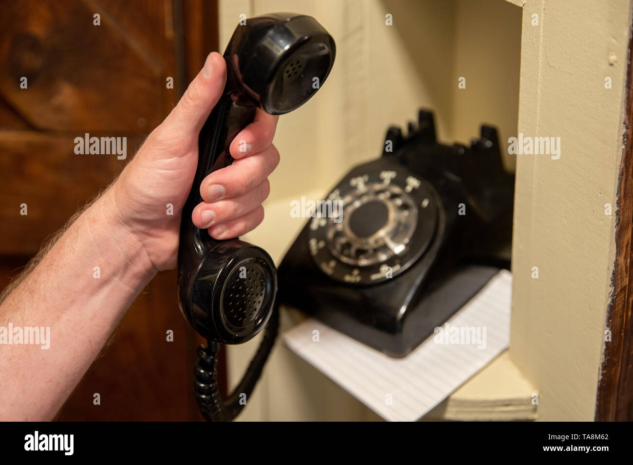 Mano che tiene il ricevitore del vecchio nero telefono rotante nel corridoio di nook telefono Foto Stock