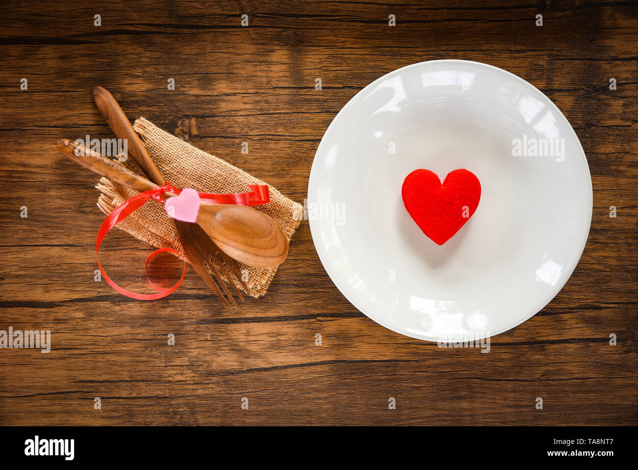 Valentines dinner romantic love food and love cooking concept - Romantic table setting decorated with wooden fork spoon and red heart on plate on dini Foto Stock