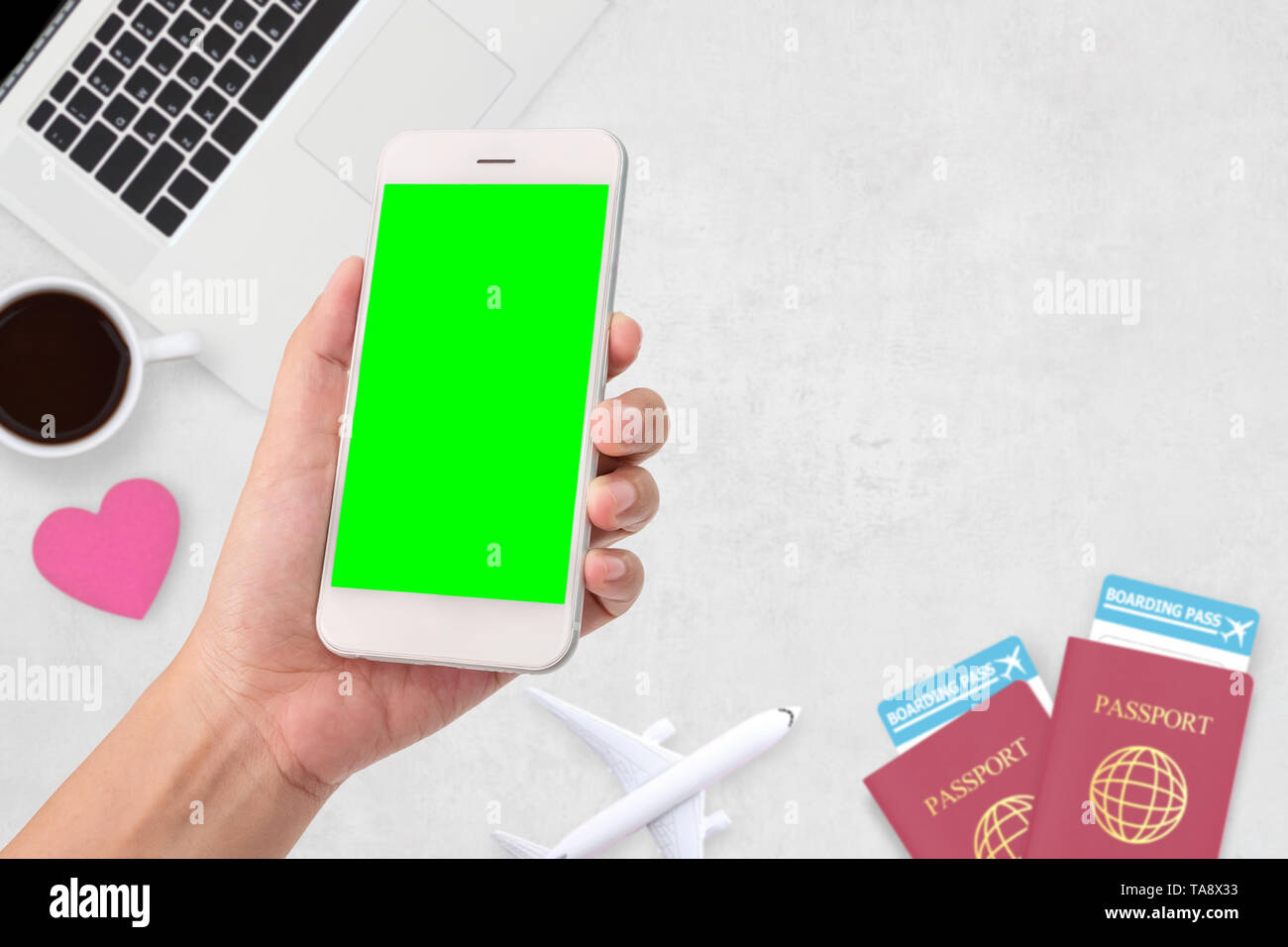 Donna mano che tiene un moderno mobile smart phone con vuoto nella schermata verde. Due passport , caffè , il computer portatile in background Foto Stock