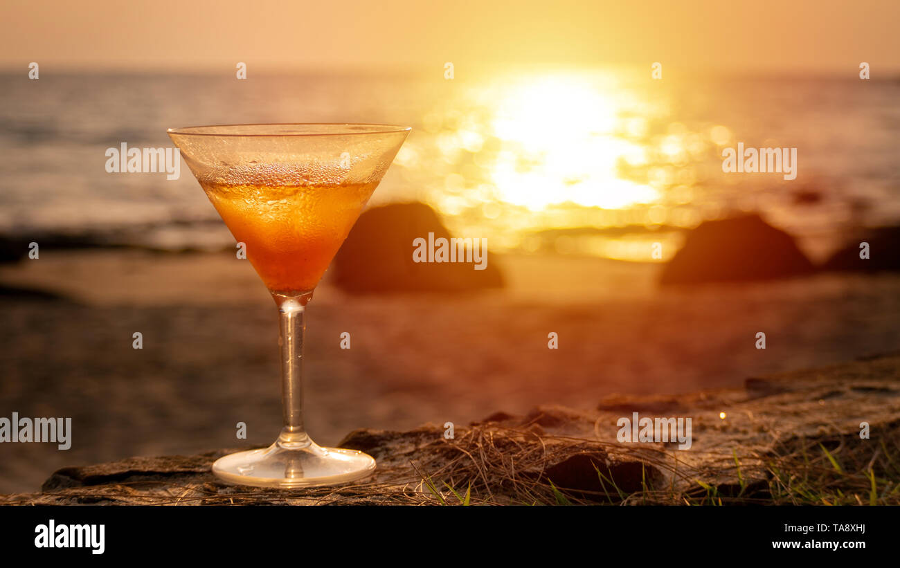 Bicchiere da cocktail sul mare con vista sulla spiaggia a sfondo durante il tramonto Foto Stock