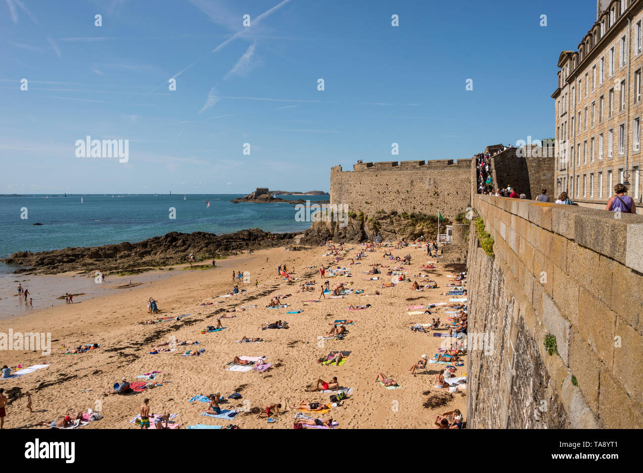 Passeggiate turistiche sui bastioni di Intra Muros Saint Malo e la gente sulla spiaggia sabbiosa, Bretagna Francia Foto Stock