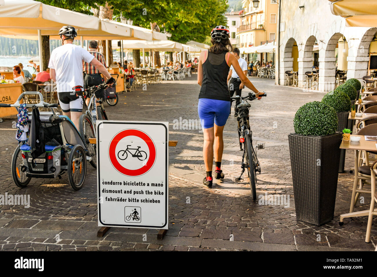 GARDA LAGO DI GARDA ITALIA - Settembre 2018: due persone osservano i requisiti sul segno di smontare e spingere le loro biciclette sul lungomare di Garda Foto Stock