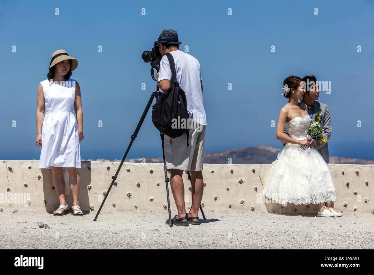 Santorini, i turisti al di sopra del mare sulla terrazza, uomo che fa foto con treppiede. Appena si sposavano giovani popoli asiatici, Grecia Europa Foto Stock