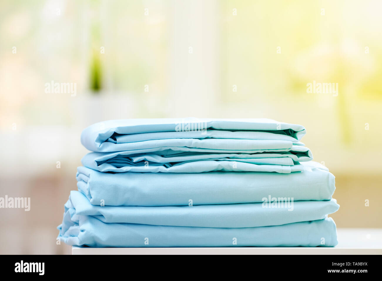 Close-up di blu biancheria da letto pulita su uno sfondo sfocato. Una pila di fogli piegati nuove lenzuola sul tavolo. La luce del sole dalla finestra. Foto Stock
