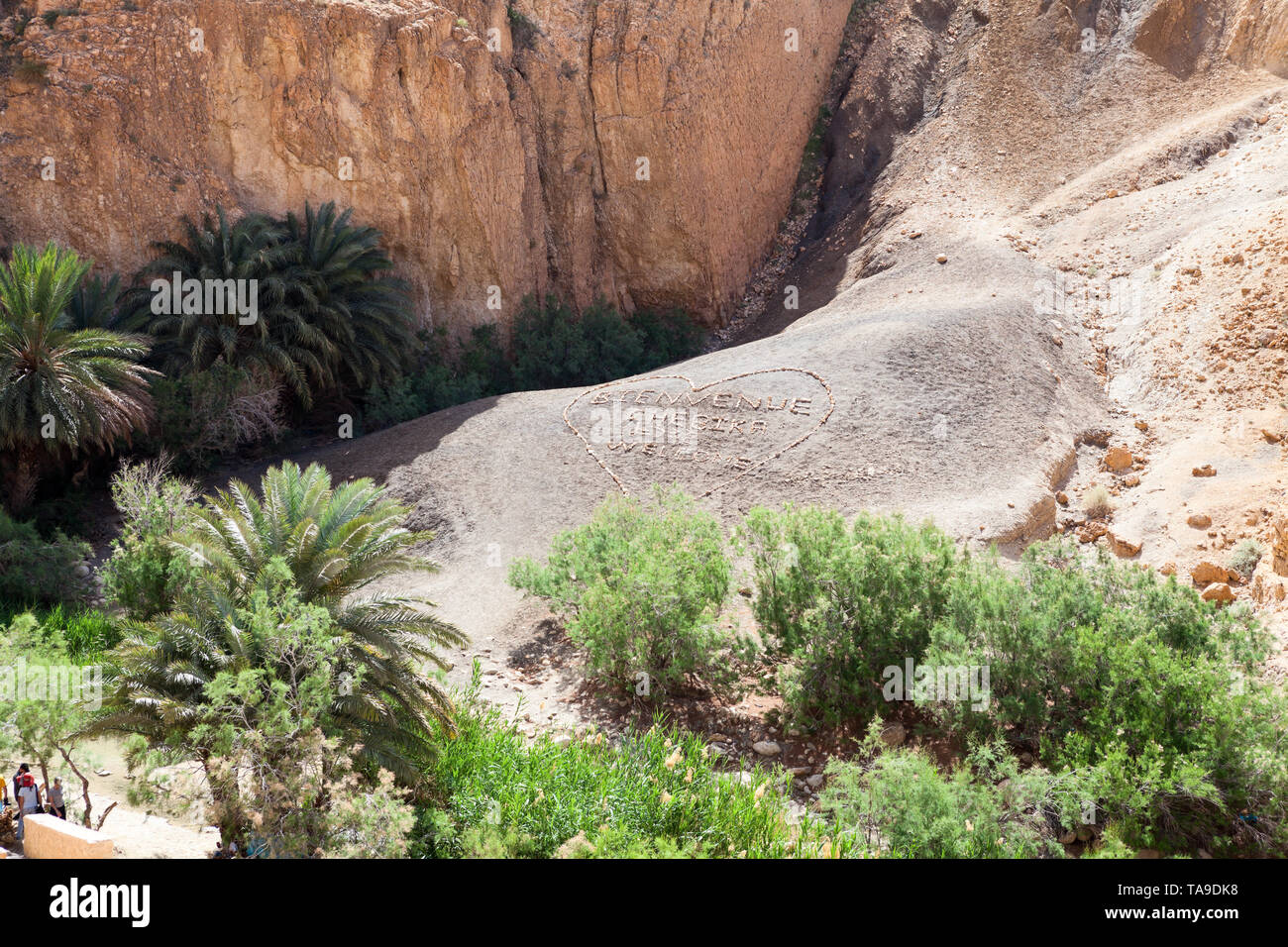 TOZEUR, TUNISIA-CIRCA NEL MAGGIO 2012: iscrizione con parole Bienvenue Chebika, benvenuto è attrazione turistica. Segno è posati sul pendio con pietre e pebbl Foto Stock