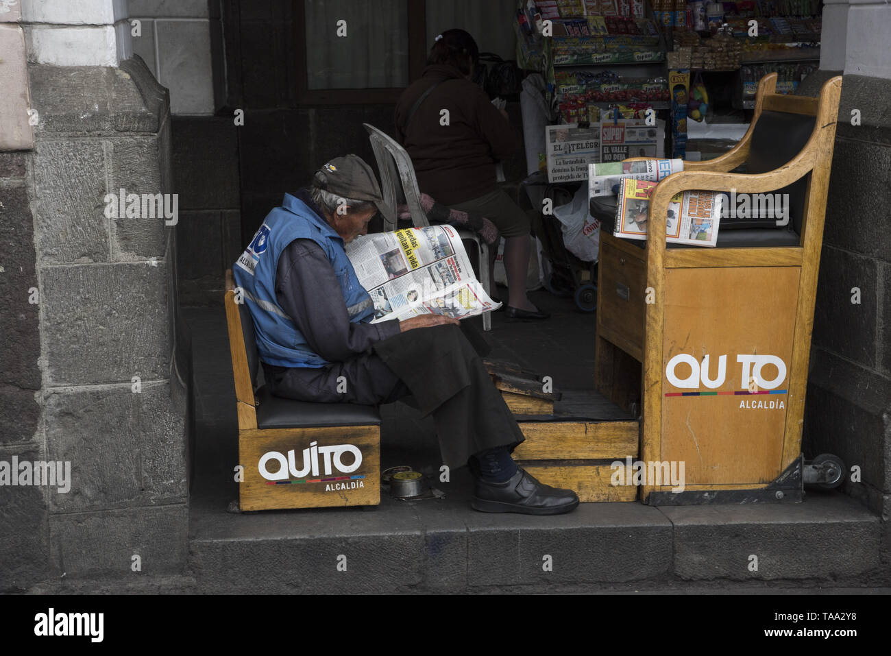 Shoeshiner in attesa di clienti e leggere il giornale in arcate del Comune di Quito presso la piazza Indipendenza di Quito in Ecuador. Foto Stock