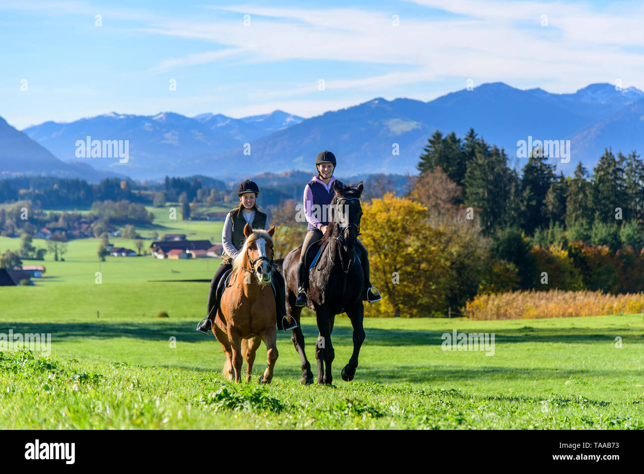Due donne sportivo in sella ai loro cavalli sul prato in Algovia bavarese Foto Stock