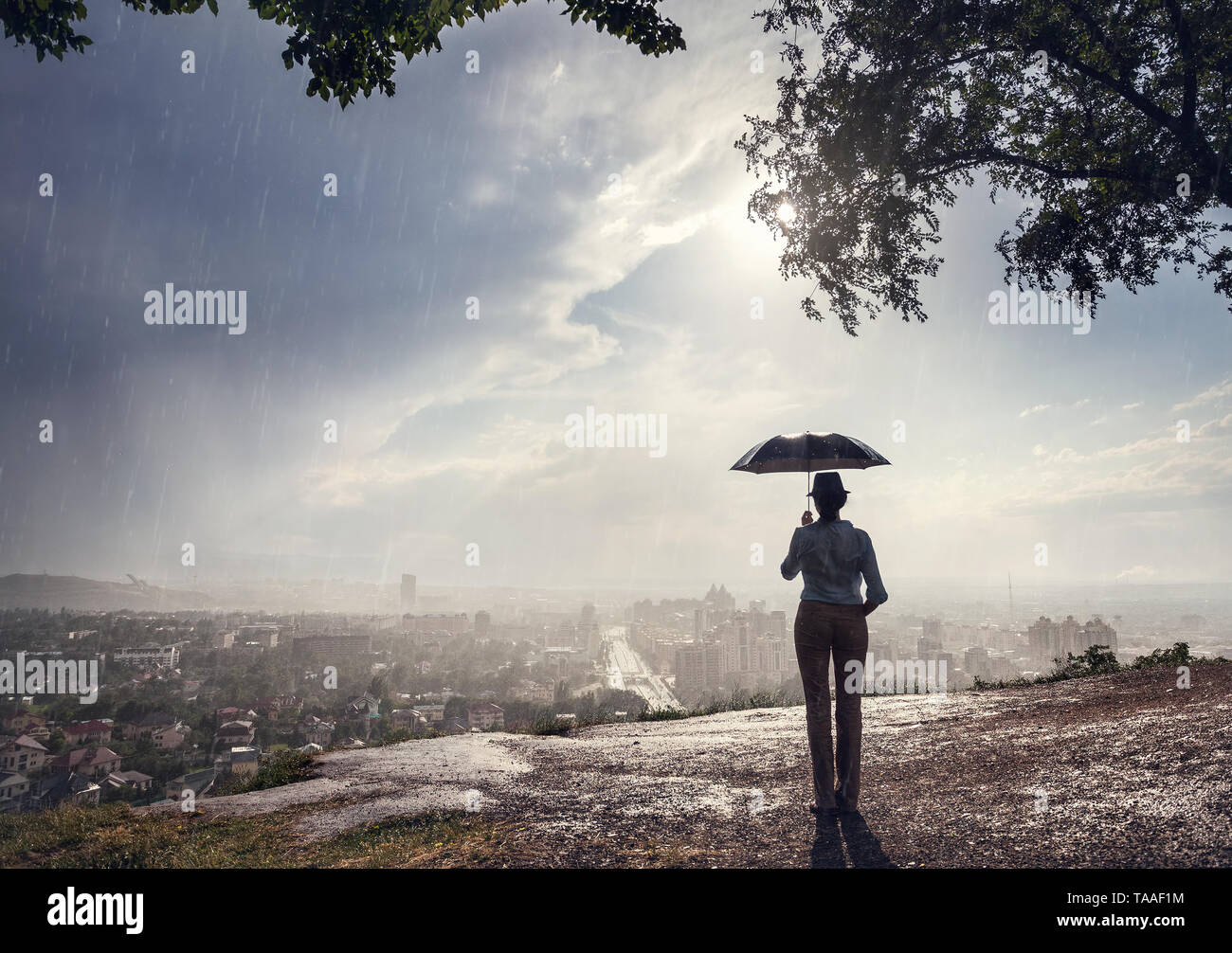 Silhouette di donna con ombrello la strada con vista sul panorama cittadino nella piovosa serata drammatica . Vintage, in stile retrò. Foto Stock